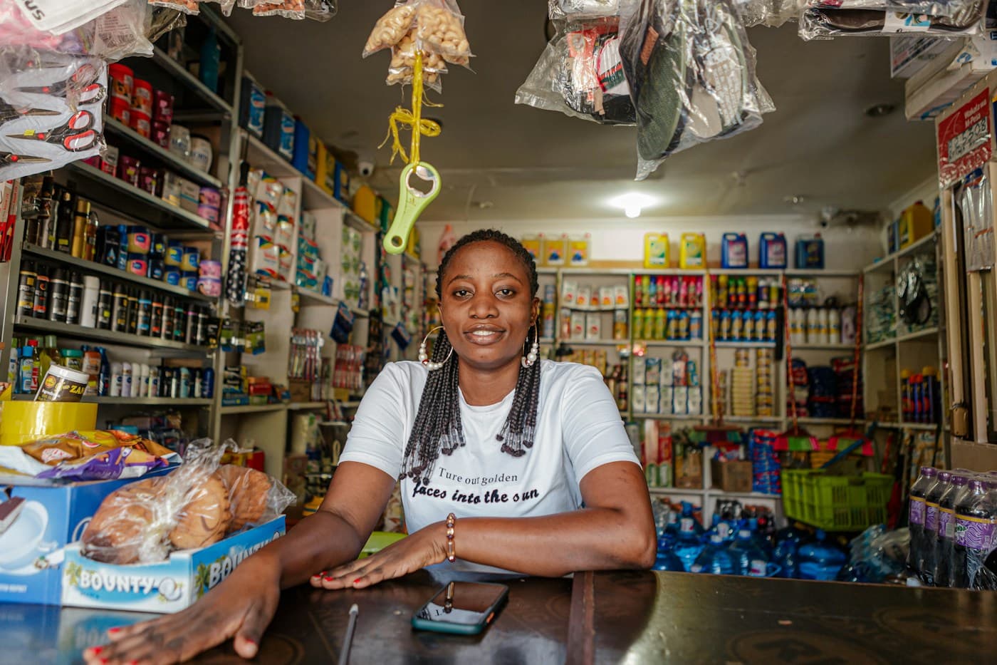 A shop owner smiling behind her counter, snacks hanging above